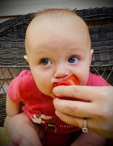 A small child experiencing the joy of bitting into a ripe tomato.