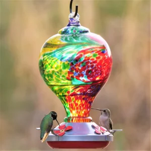 A colorful hand blown glass hummingbird feeder from musegarden.com with two resting birds enjoying the nectar.