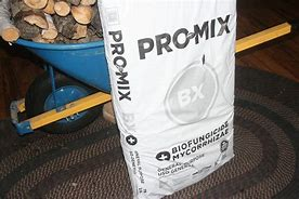 Image shows a bag of PRO-MIX soil sitting next to a wheelbarrow and some logs. 